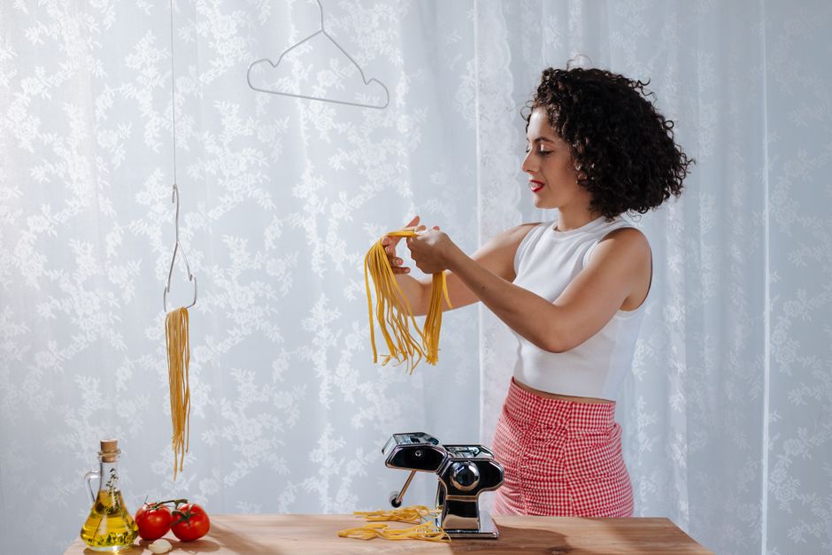 Woman making fresh Italian pasta with pasta machine and drying it indoors.