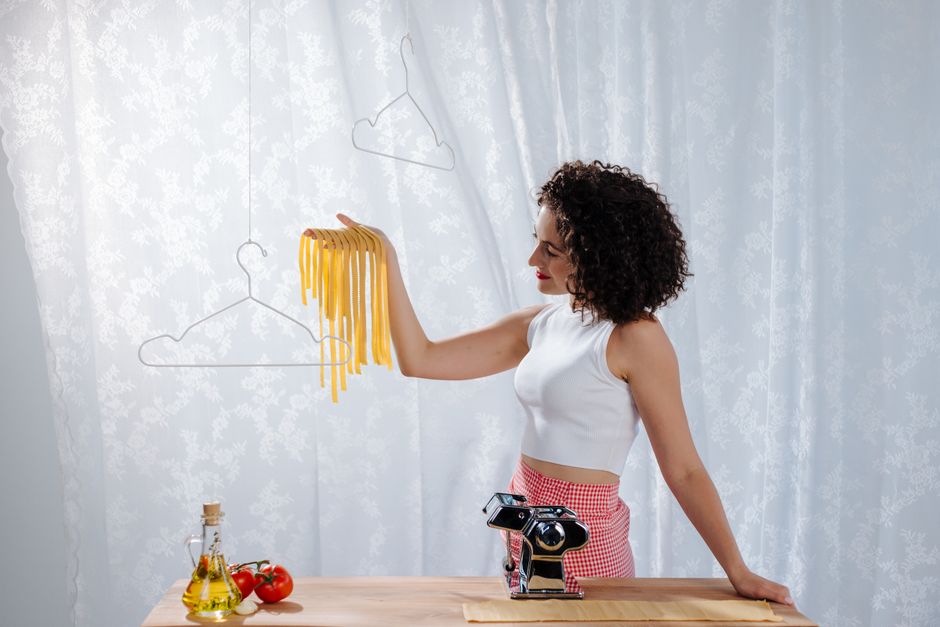 A woman proudly displays freshly made pasta hanging, showcasing home cooking skills.
